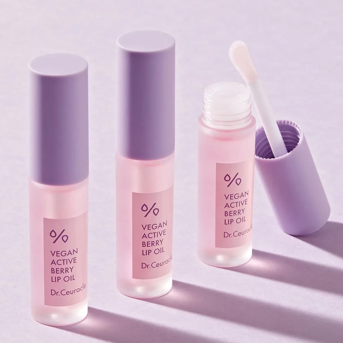 Three bottles of Dr. Ceuticals Vegan Active Berry Lip Oil on a light purple background