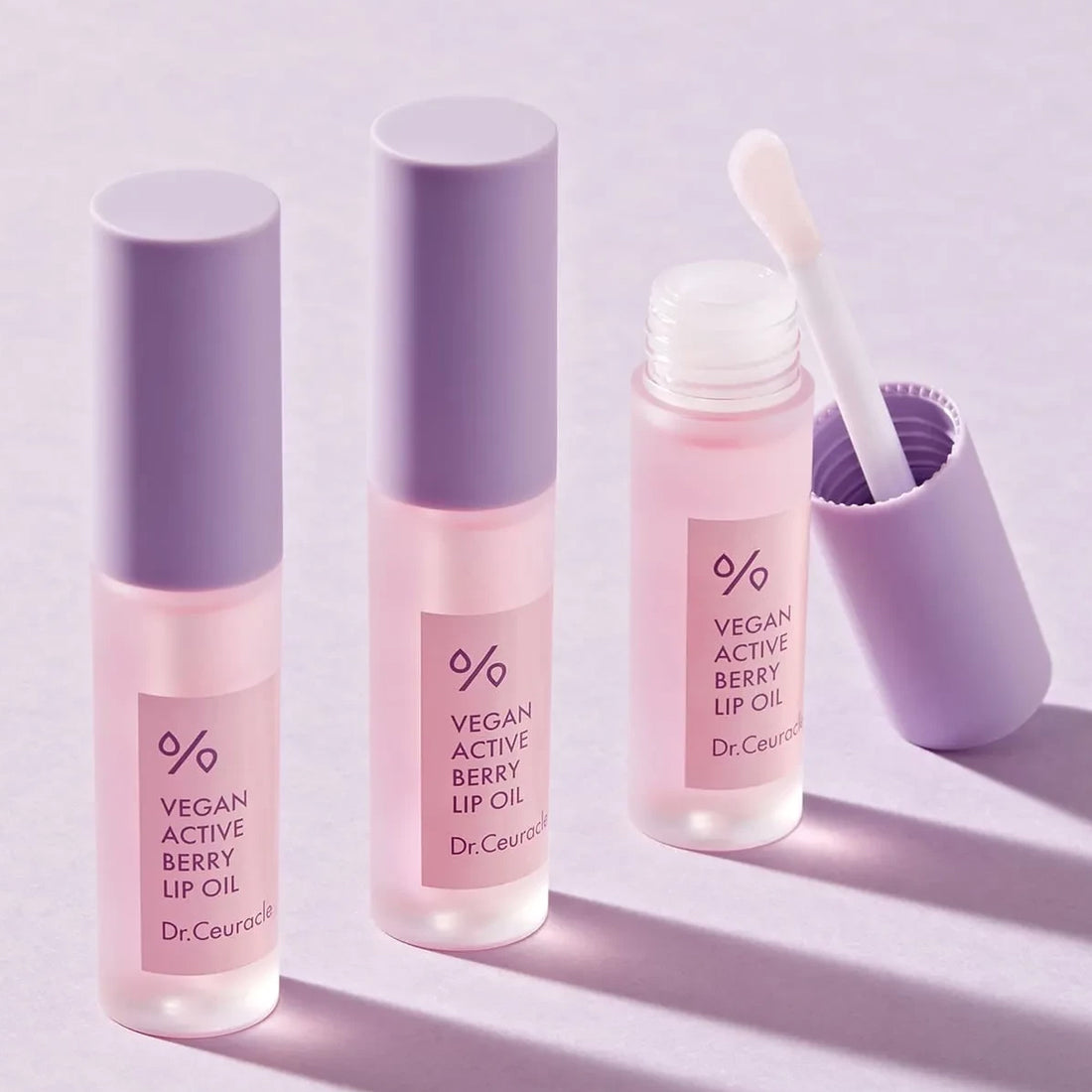 Three bottles of Dr. Ceuticals Vegan Active Berry Lip Oil on a light purple background