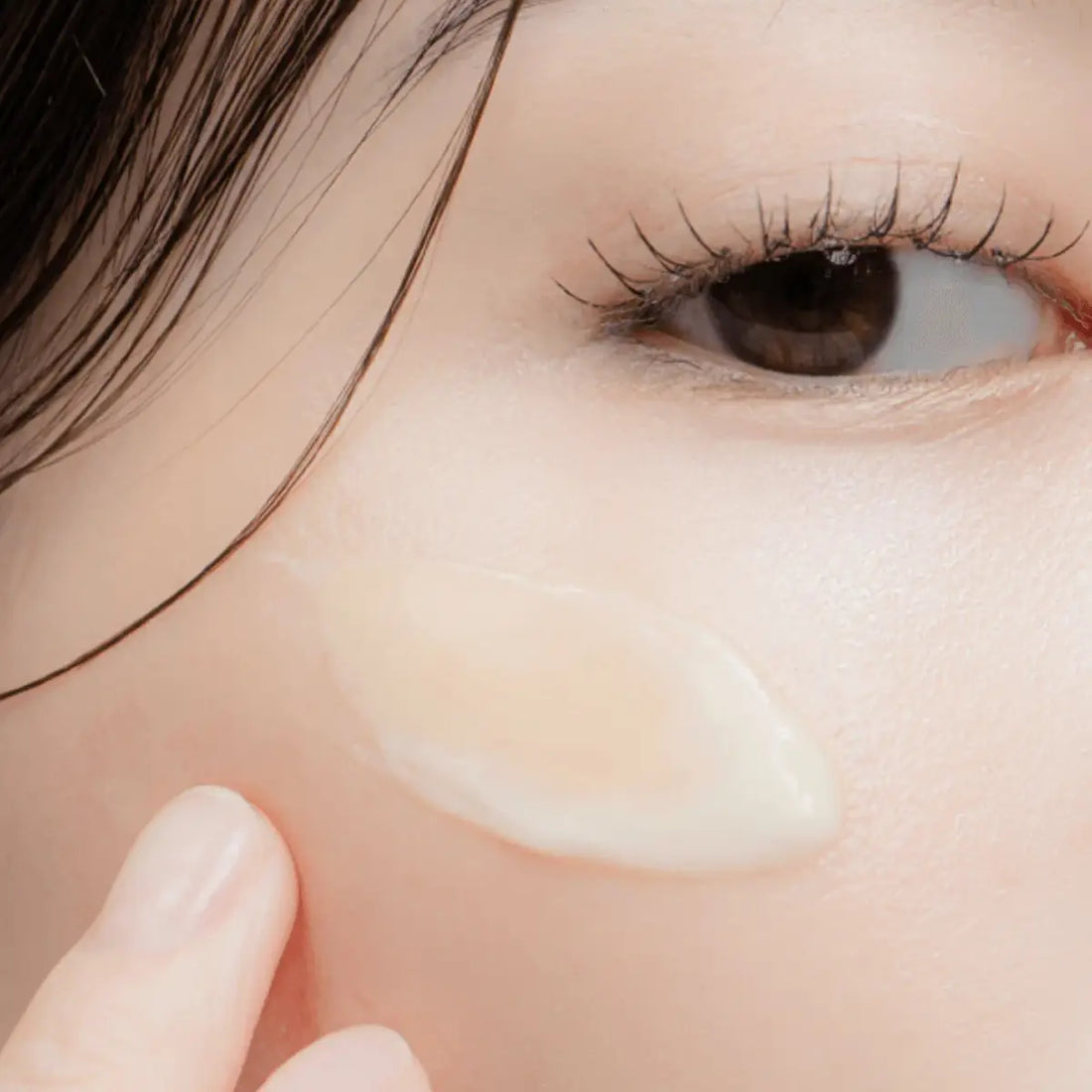 Close-up of a person applying cream under their eye with a finger.