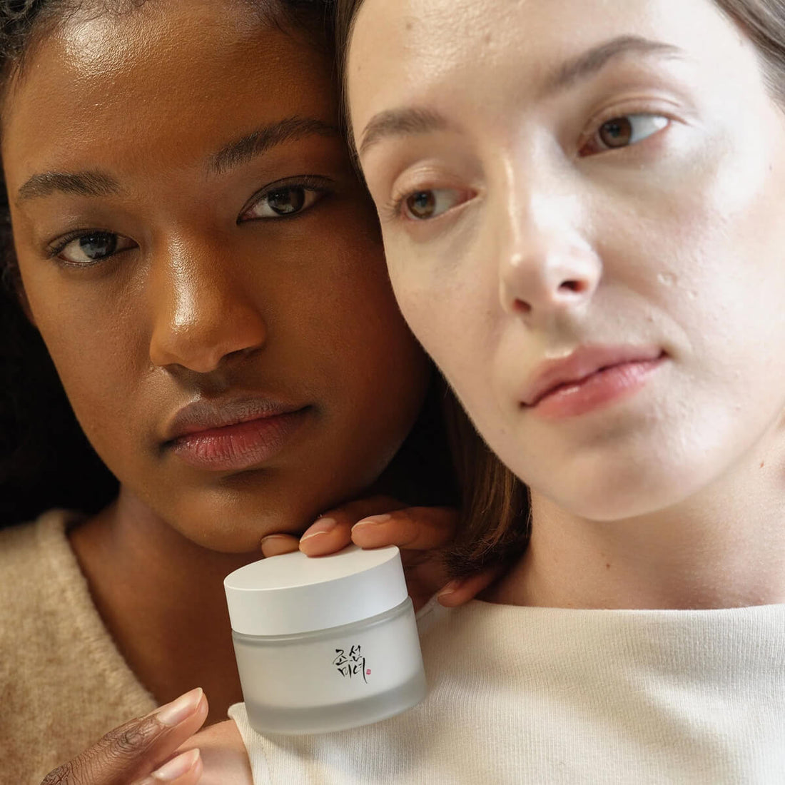 Two women holding a jar of cream against a neutral background