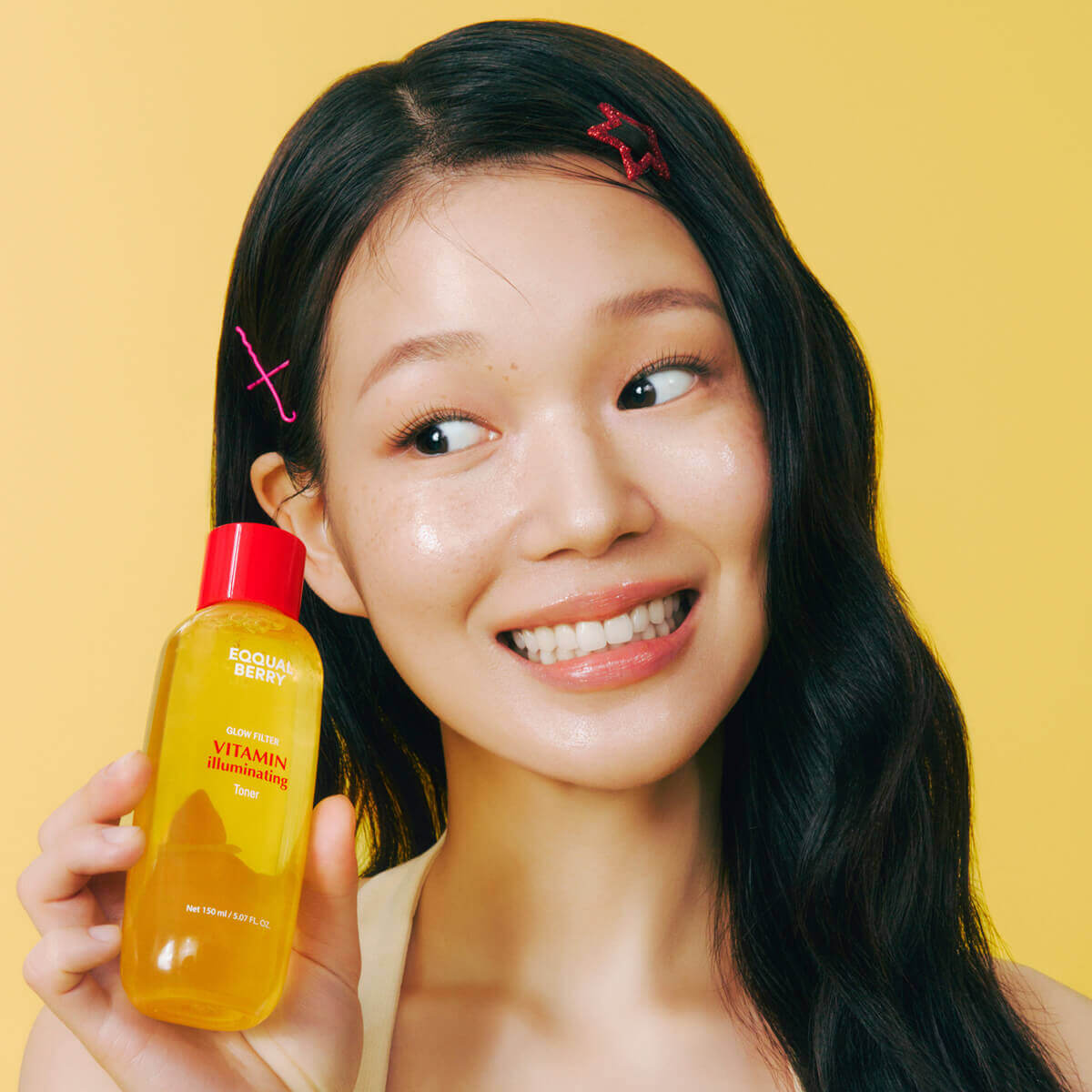 Young woman holding Eqqualberry Vitamin Illuminating Toner (150mL) with a bright smile against a yellow background.