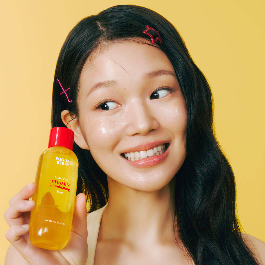 Young woman holding Eqqualberry Vitamin Illuminating Toner (150mL) with a bright smile against a yellow background.