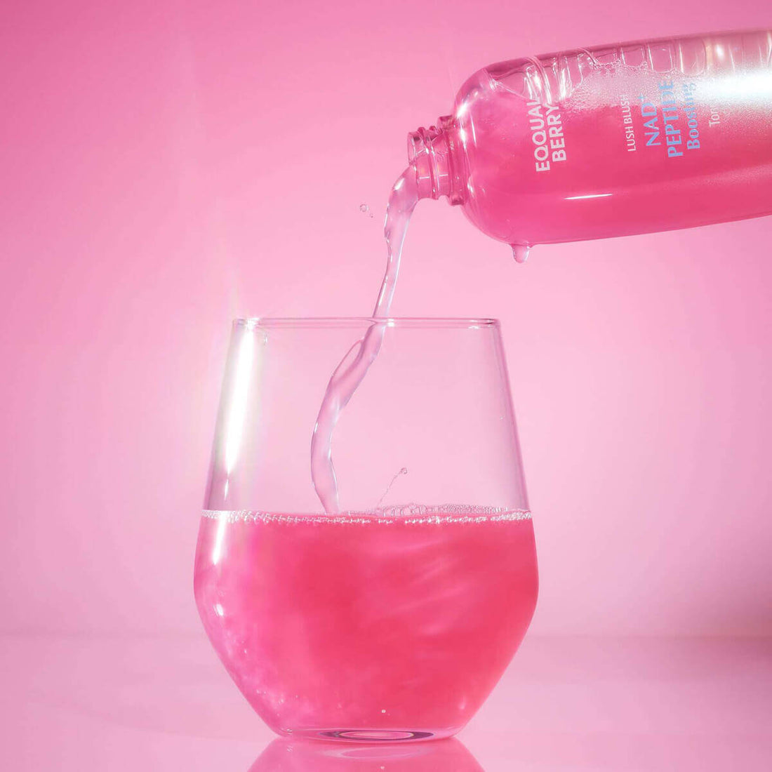 Pouring Eqqualberry NAD+ Peptide Boosting Toner into a glass, showcasing its vibrant pink color.