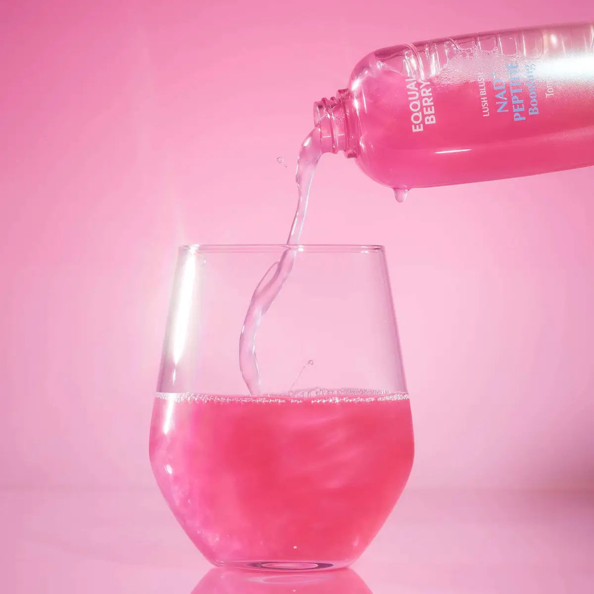 Pink drink being poured from a Eqqualberry NAD+ Peptide Boosting Toner into a glass against a pink background