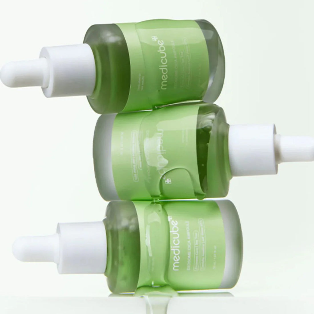 Green skincare serum bottles with white caps on a reflective surface