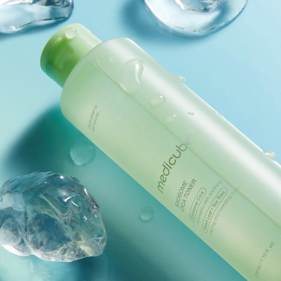 Green bottle of Medicube Emulsion Cica Water on a blue background with water droplets.