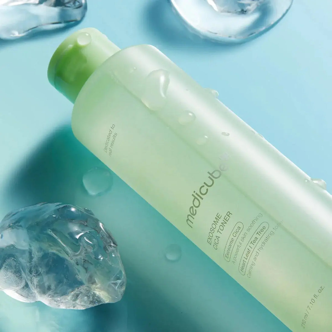 Green bottle of Medicube Exfoliate Toner on a blue background with water droplets.