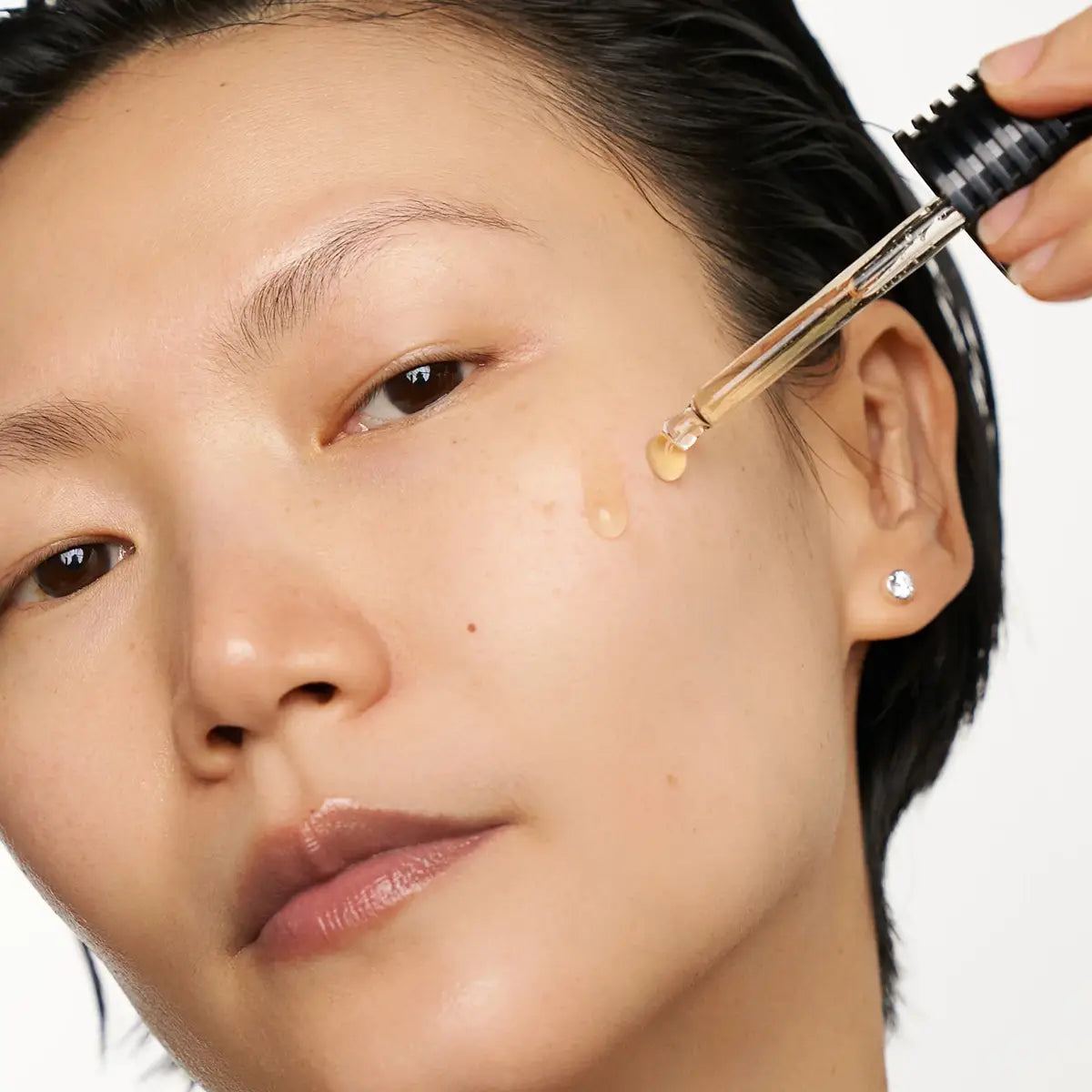 Person applying a droplet of liquid to their face using a dropper.