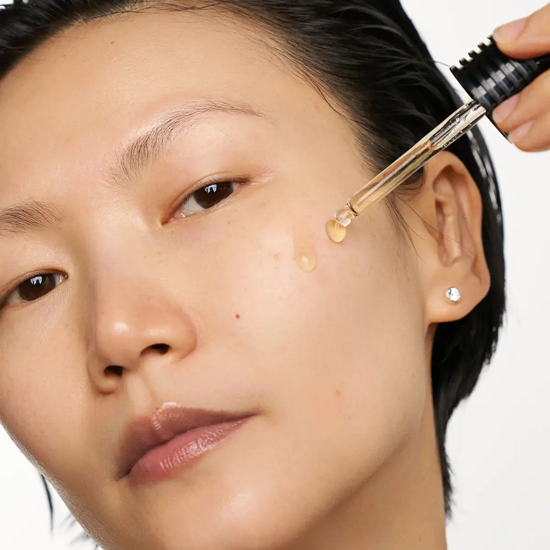 Person applying a droplet of liquid to their face using a dropper.