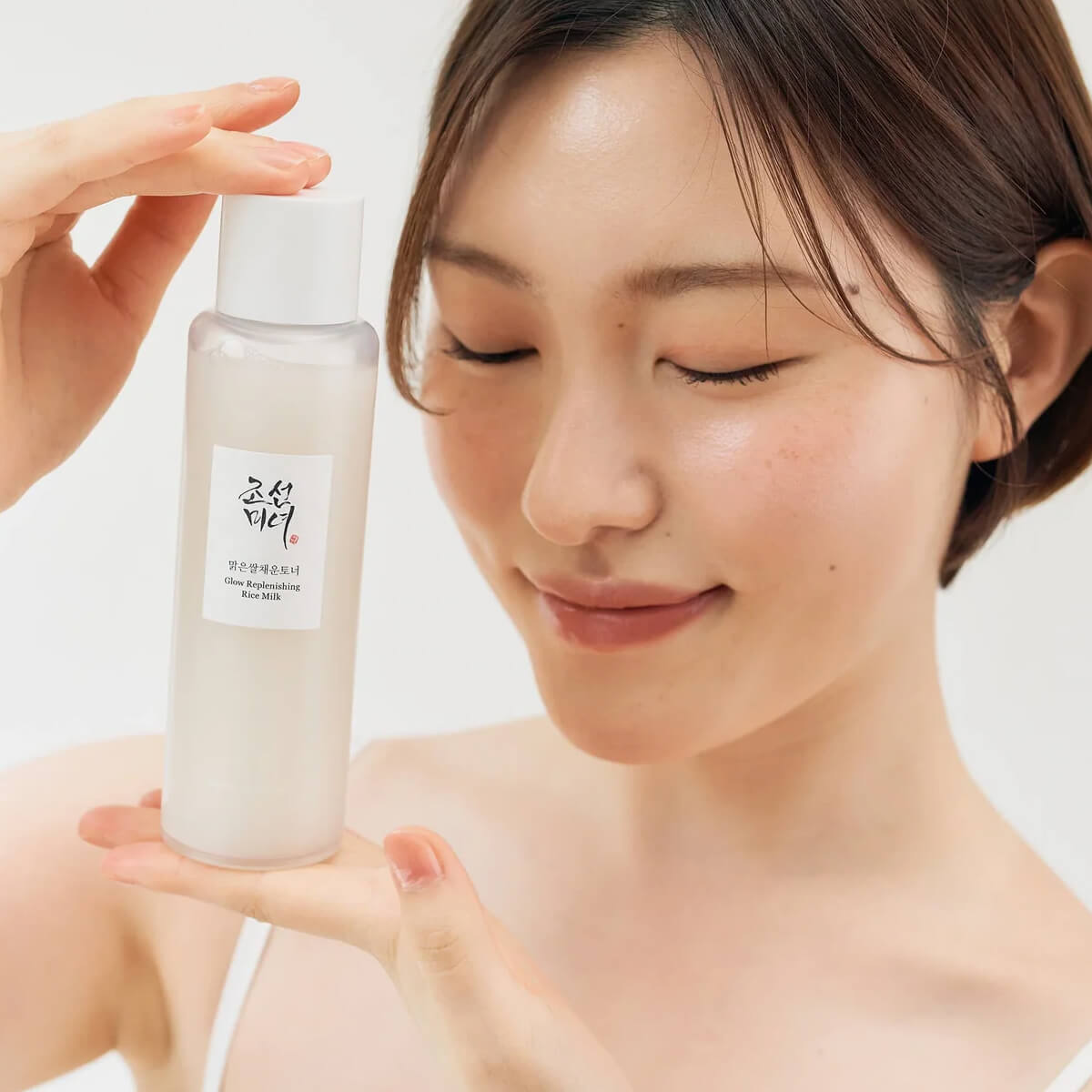 Woman holding a skincare product with a plain background