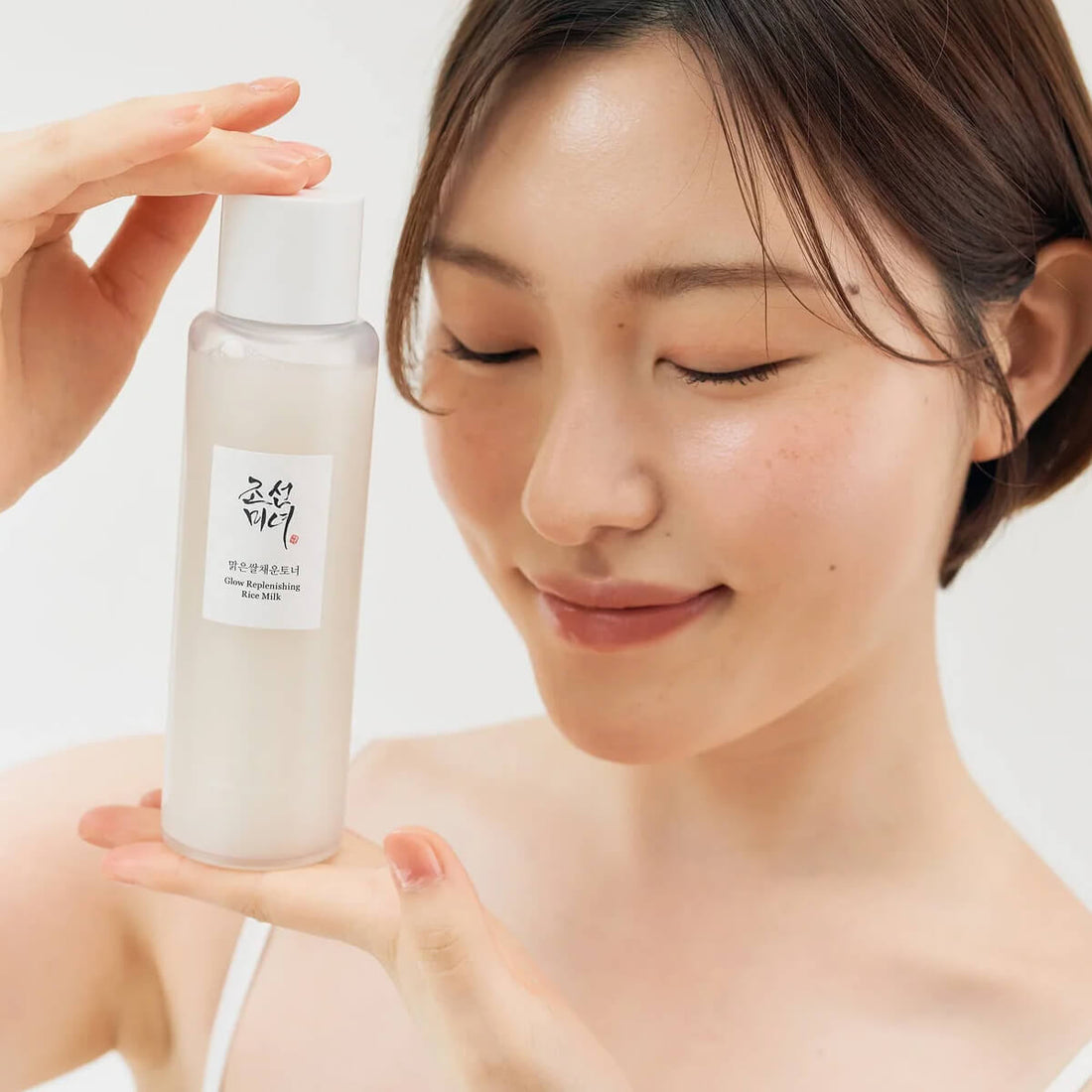 Woman holding a skincare product with a plain background