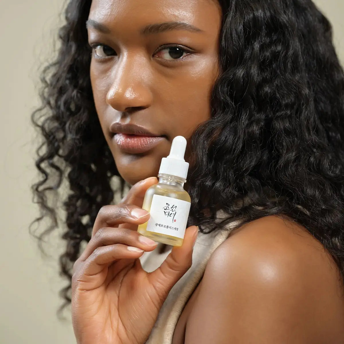 Woman holding a skincare product bottle with a neutral background