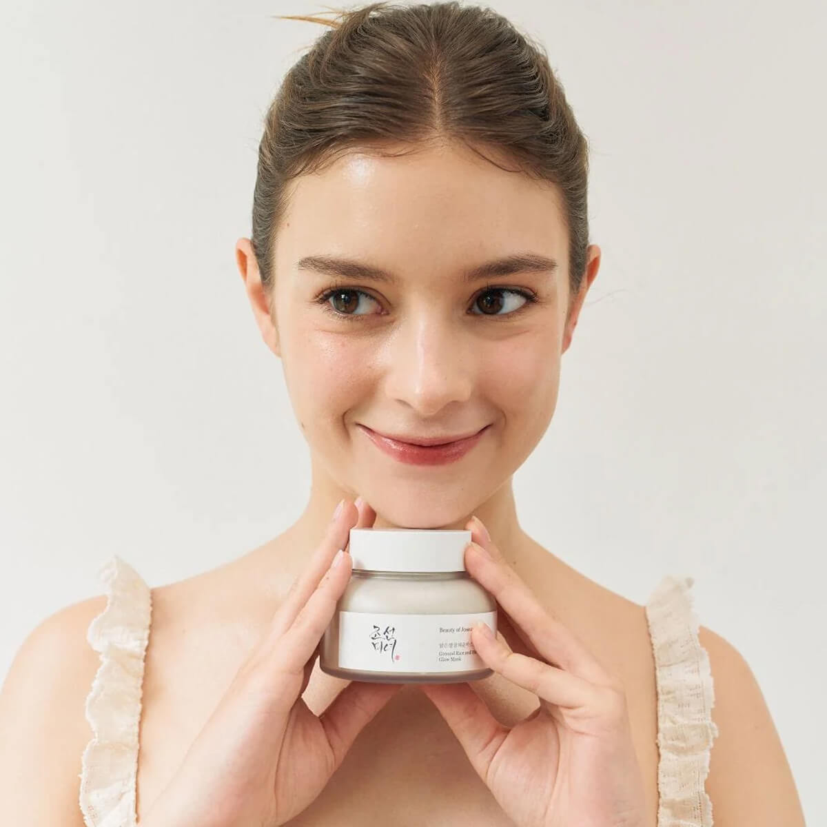 Woman holding a jar of cream against a plain background