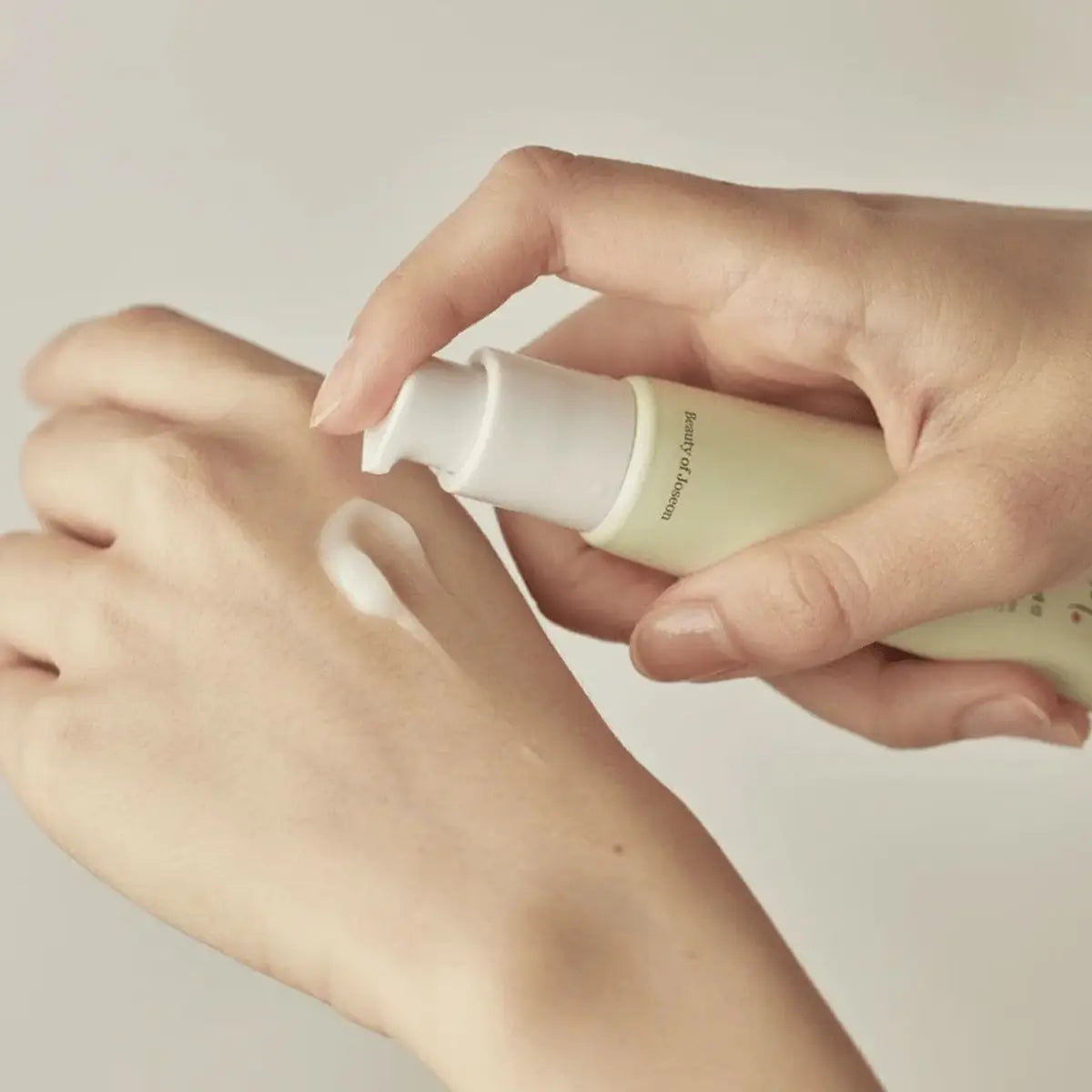 Hand applying a Beauty of Joseon Light On Serum Centella Vitamin C to another hand against a neutral background