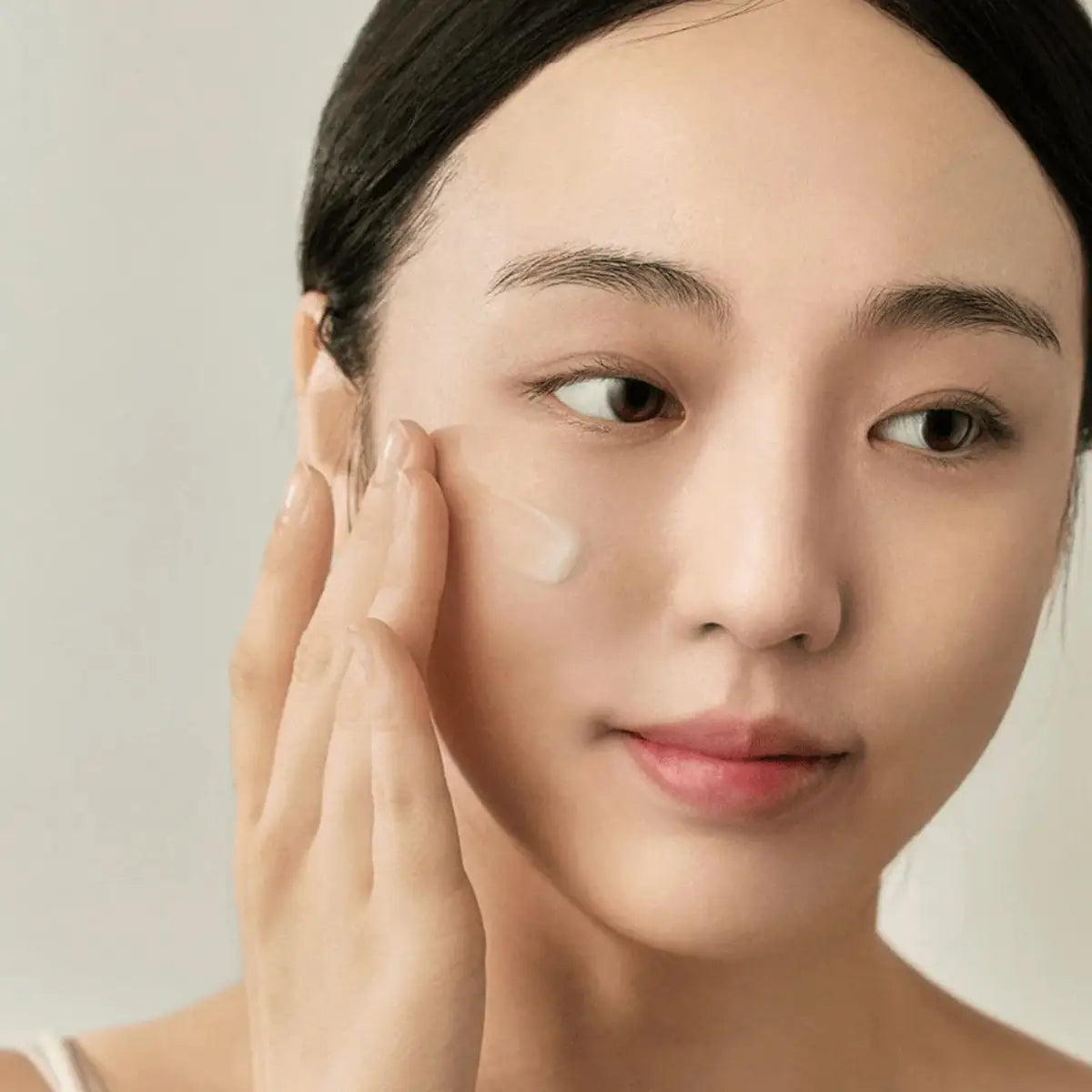 Woman applying Beauty of Joseon Light On Serum Centella Vitamin C to her face with a neutral background