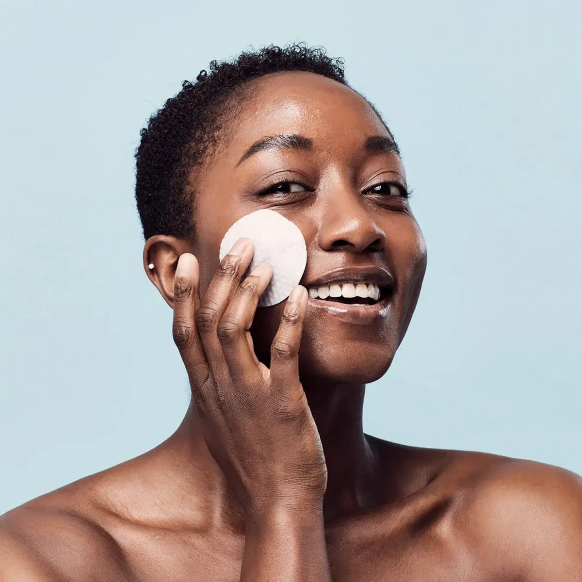 Woman applying Medicube Zero Pore Pad to her face with a cotton pad against a light blue background