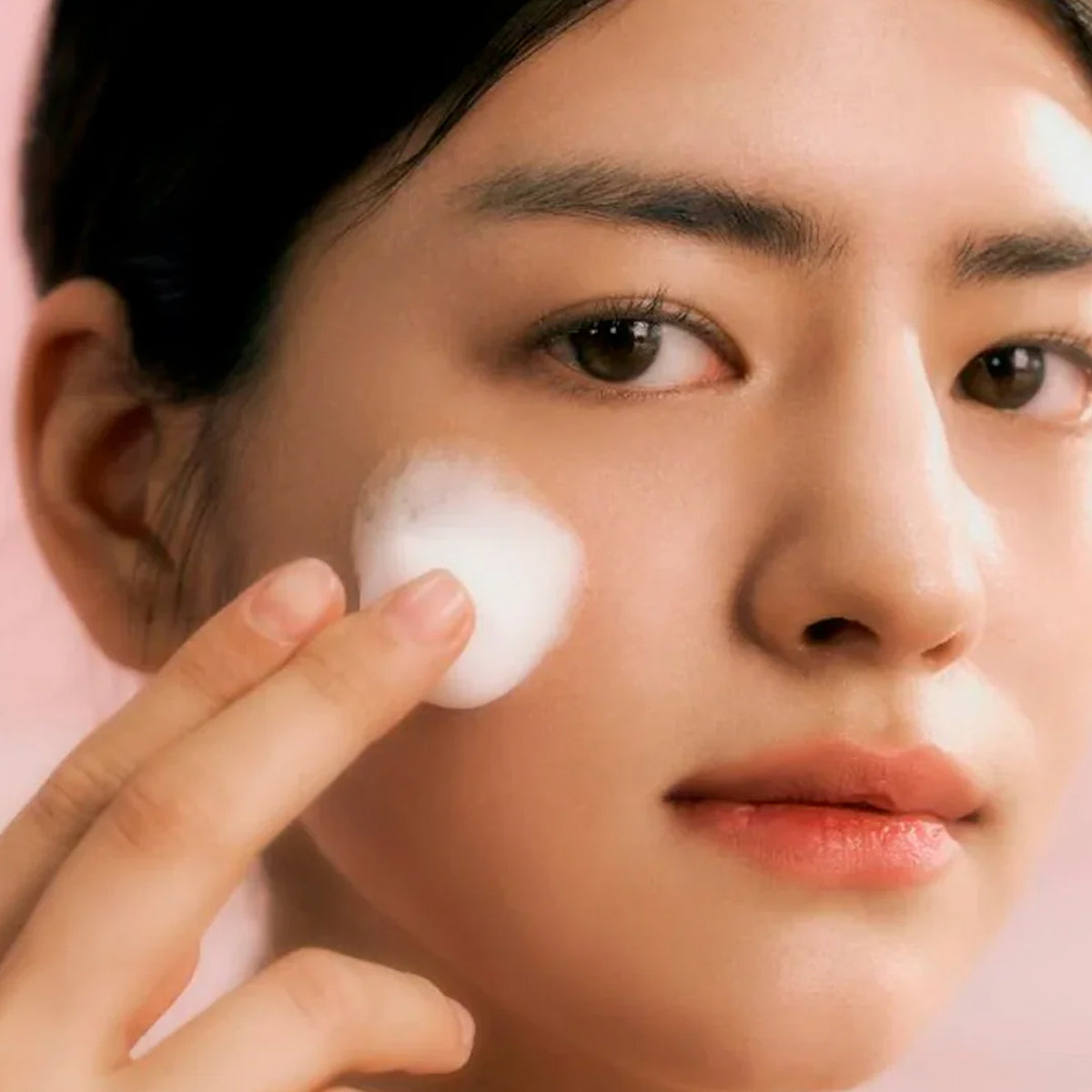 Person applying white cream to their face with a pink background