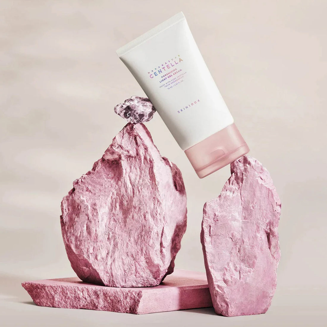 Pink skincare product on a pink rock with a beige background