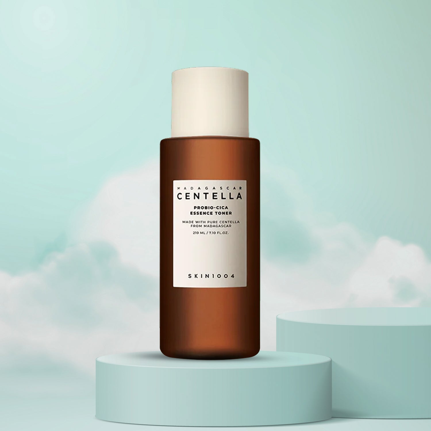 A bottle of Madagascar Centella Probio-Cica Essence Toner by Skin1004, presented on a pedestal with a cloudy sky background.