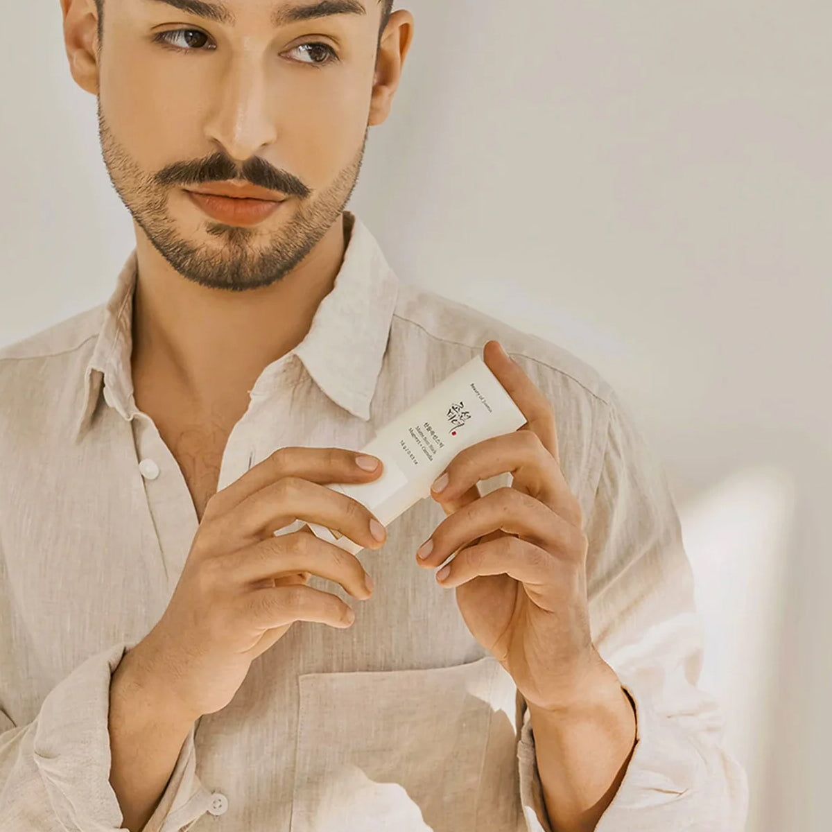 Man holding a skincare product in a neutral setting