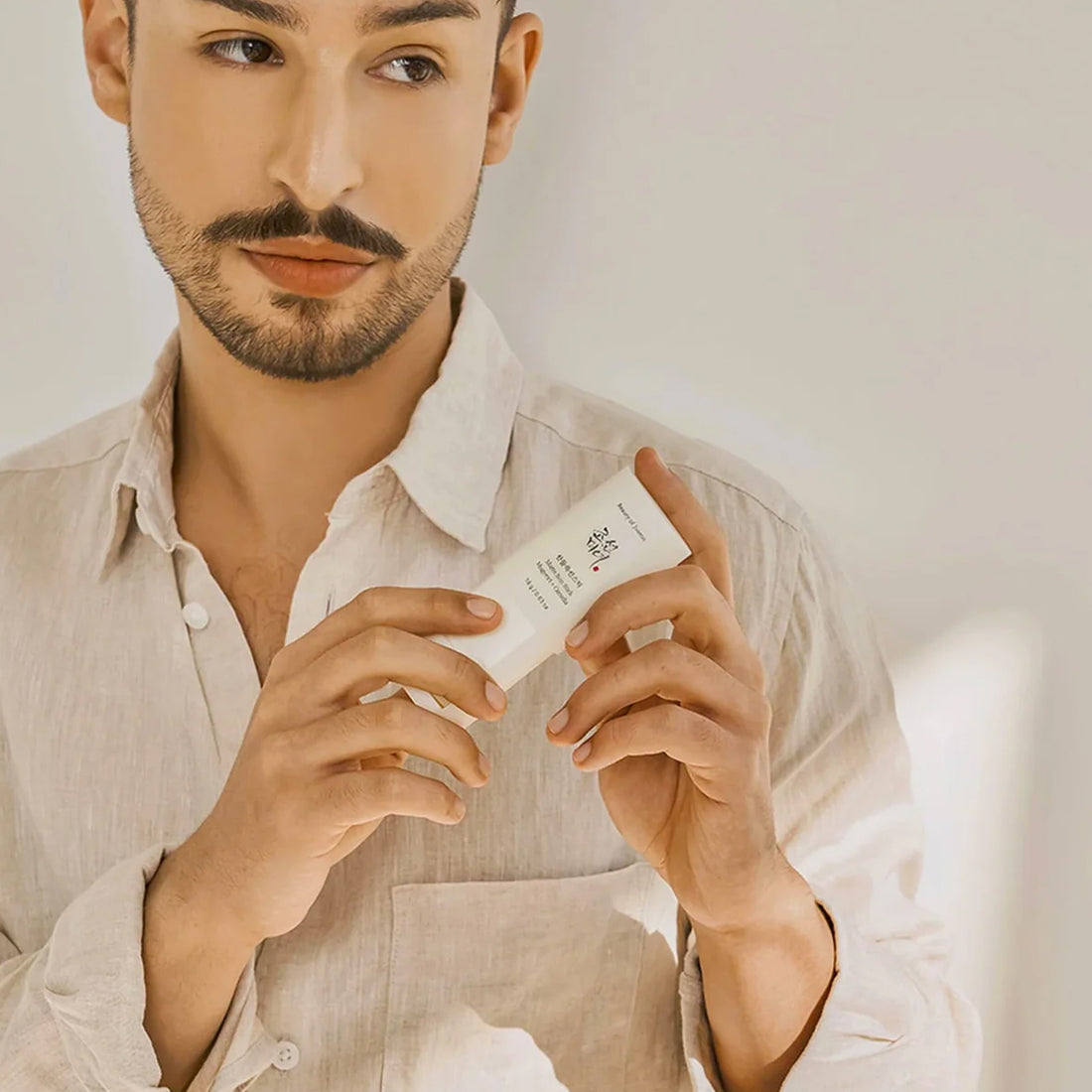 Man holding a skincare product in a neutral setting