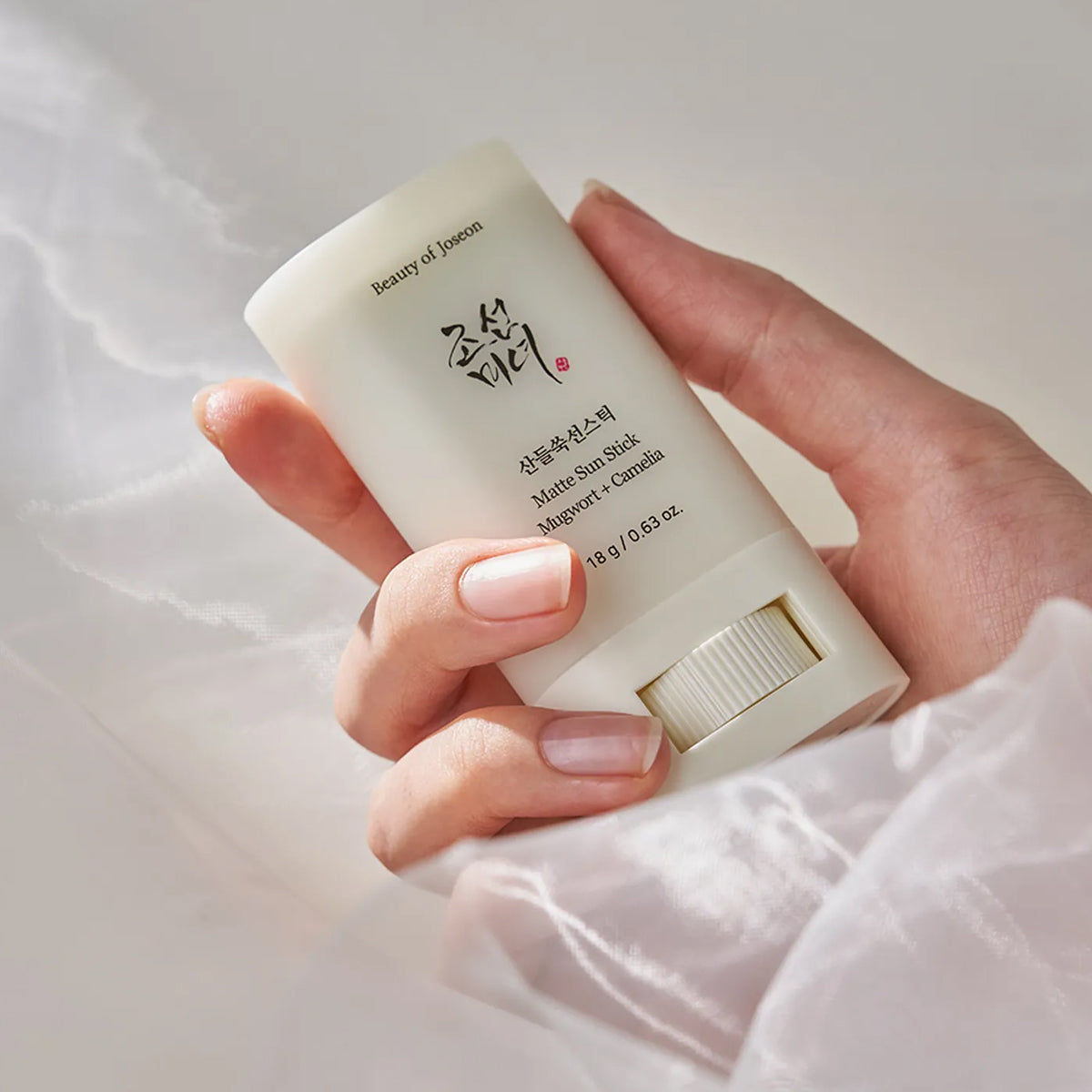 Hand holding a white sun stick with visible branding against a light background