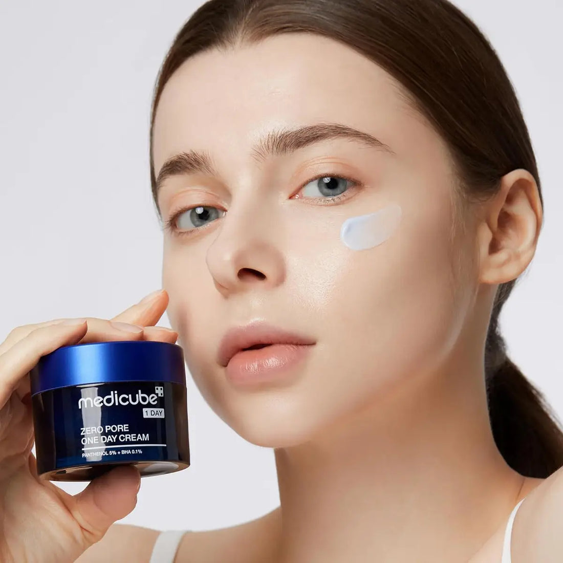 Woman applying cream to her face with a Medicube jar in the foreground