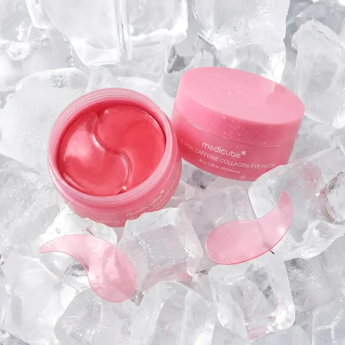 Pink medicube caffeine collagen eye patch cream shown open with two pink eye patches resting beside it, surrounded by clear ice cubes.