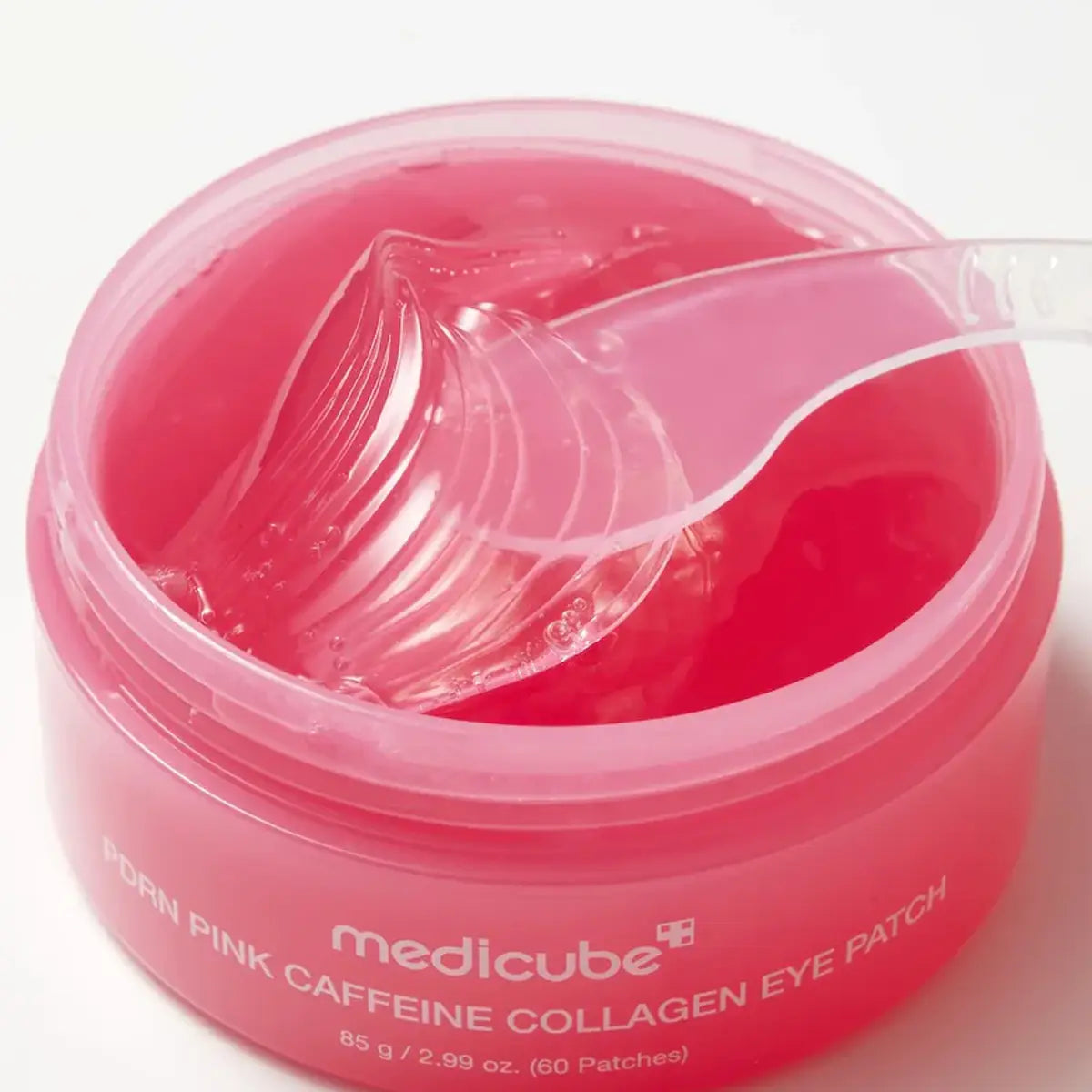 An open jar of medicube Porn Pink Caffeine Collagen Eye Patch with a clear plastic spoon showing the translucent pink gel inside, on a white background.