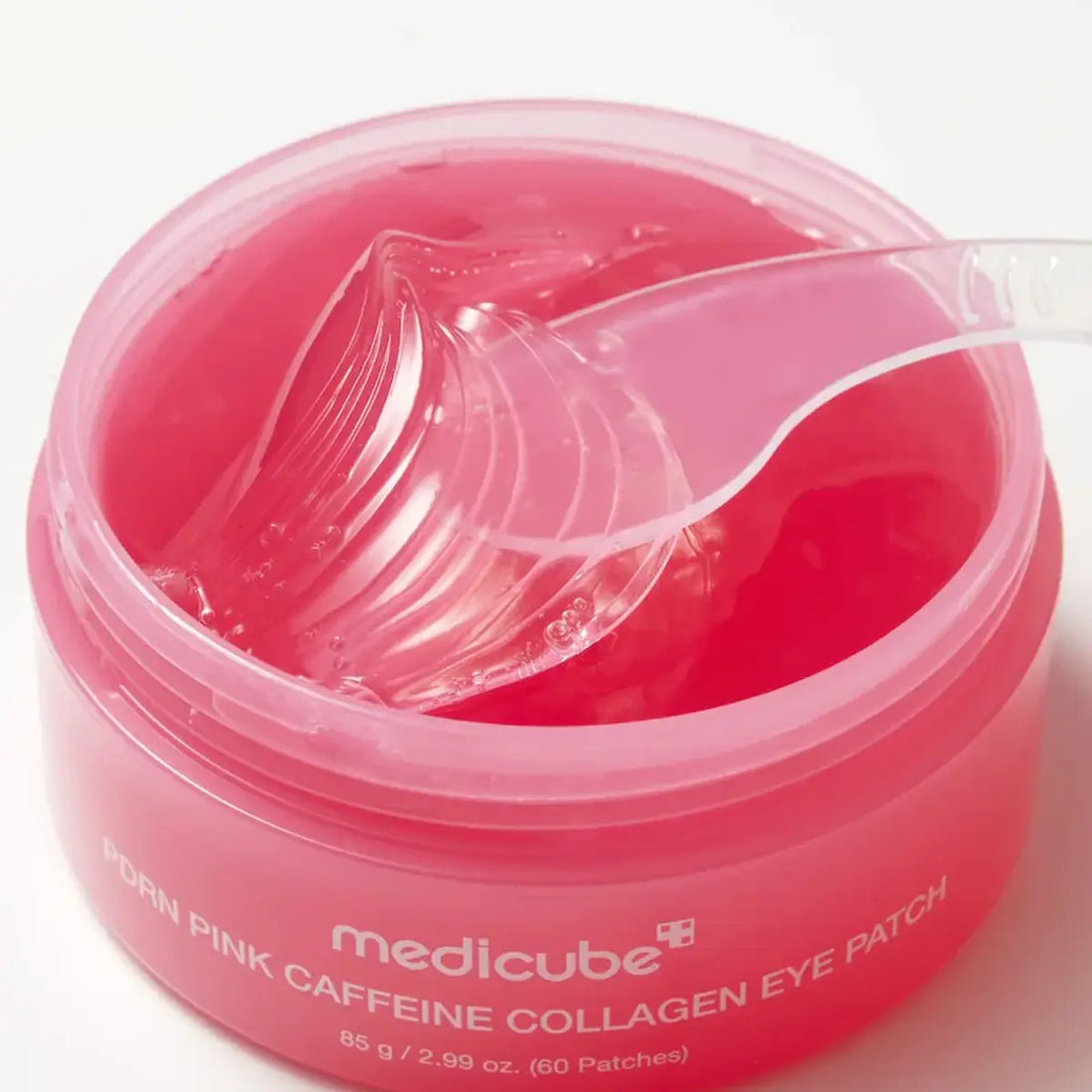 An open jar of medicube Porn Pink Caffeine Collagen Eye Patch with a clear plastic spoon showing the translucent pink gel inside, on a white background.