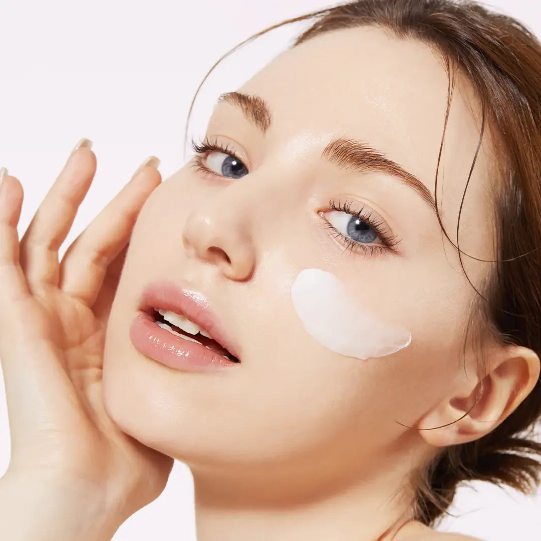 Woman applying cream to her face with a white background