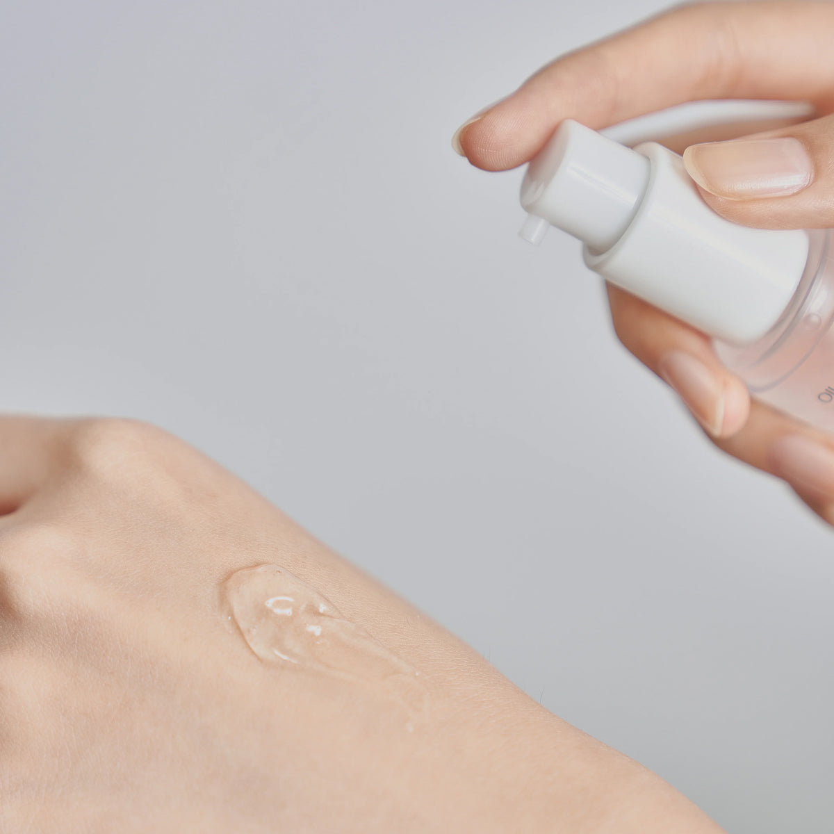 Hand applying a clear liquid to skin with a small bottle on a light gray background
