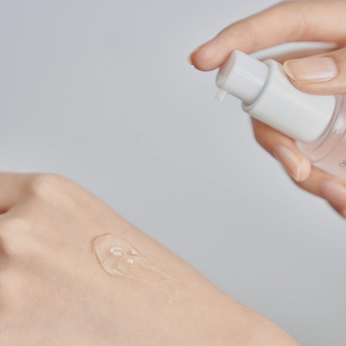 Hand applying a clear liquid to skin with a small bottle on a light gray background