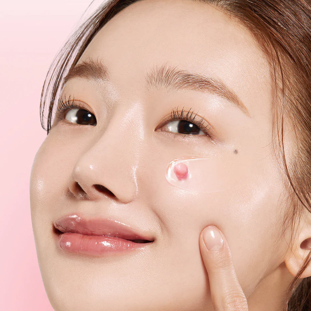 Close-up of a woman applying cream to her face with a pink background