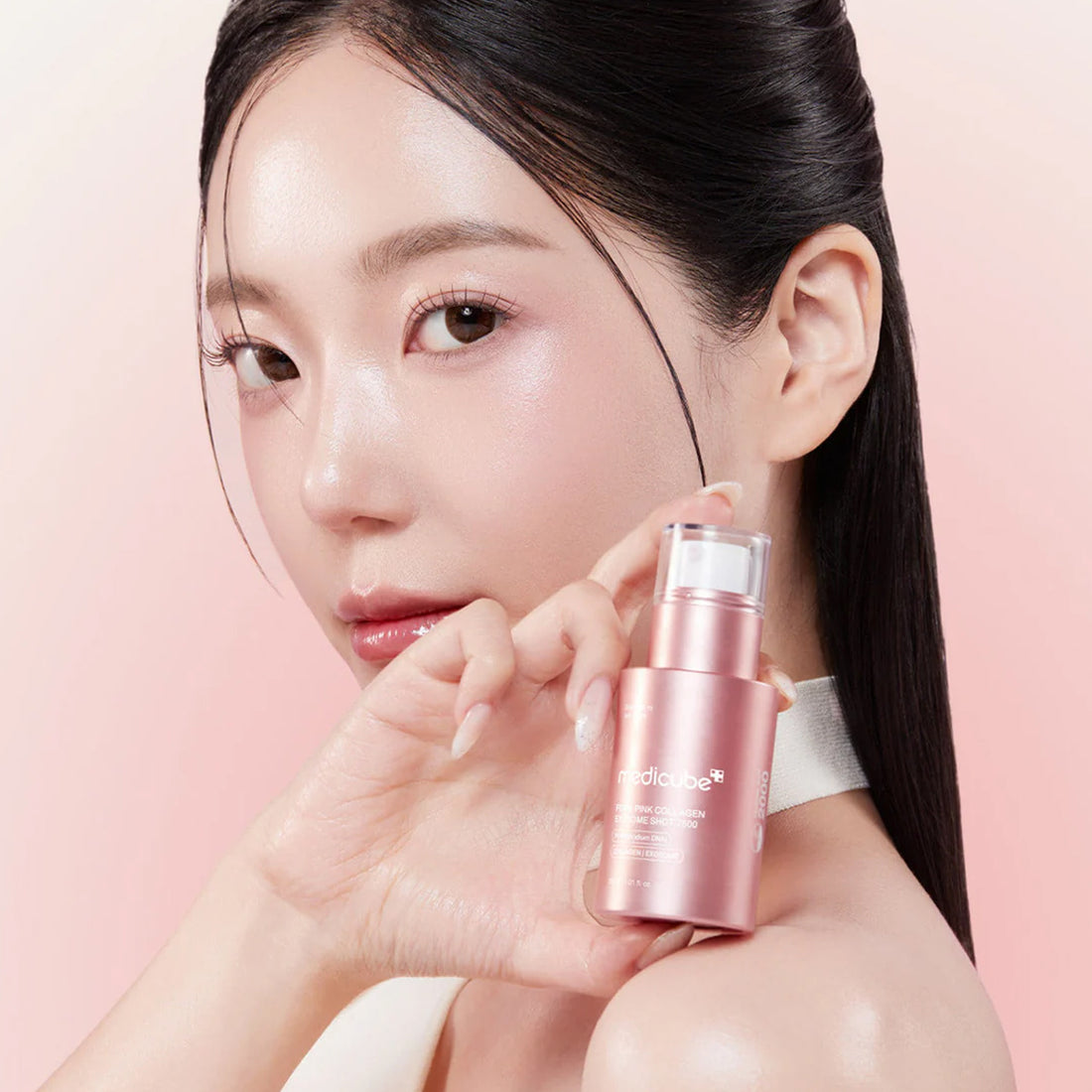 Woman holding a pink skincare bottle against a pink background