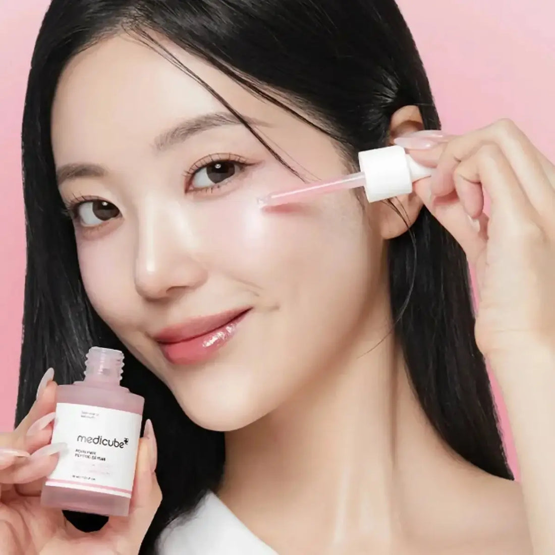 Woman applying skincare product with a dropper and bottle against a pink background