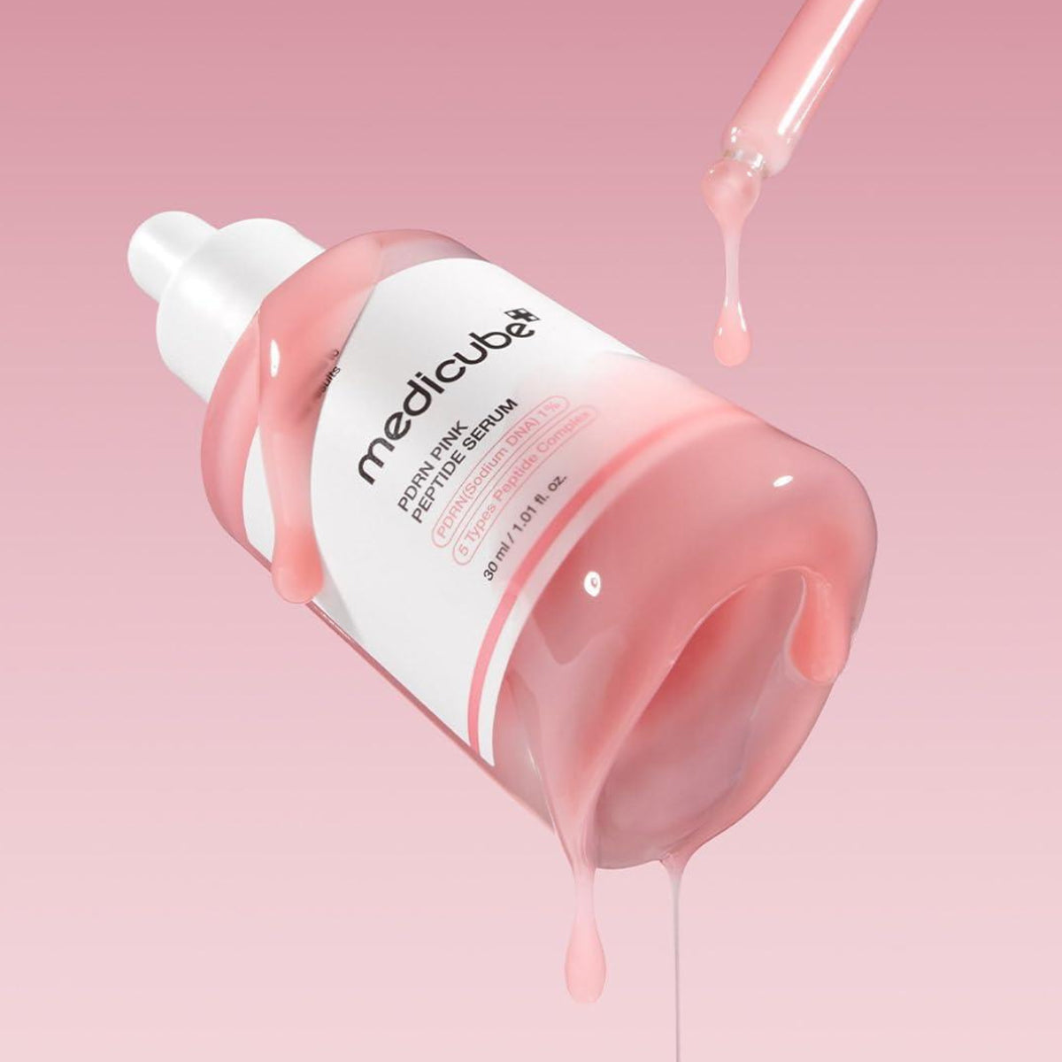 Medicube serum bottle with pink serum being dripped onto a pink background