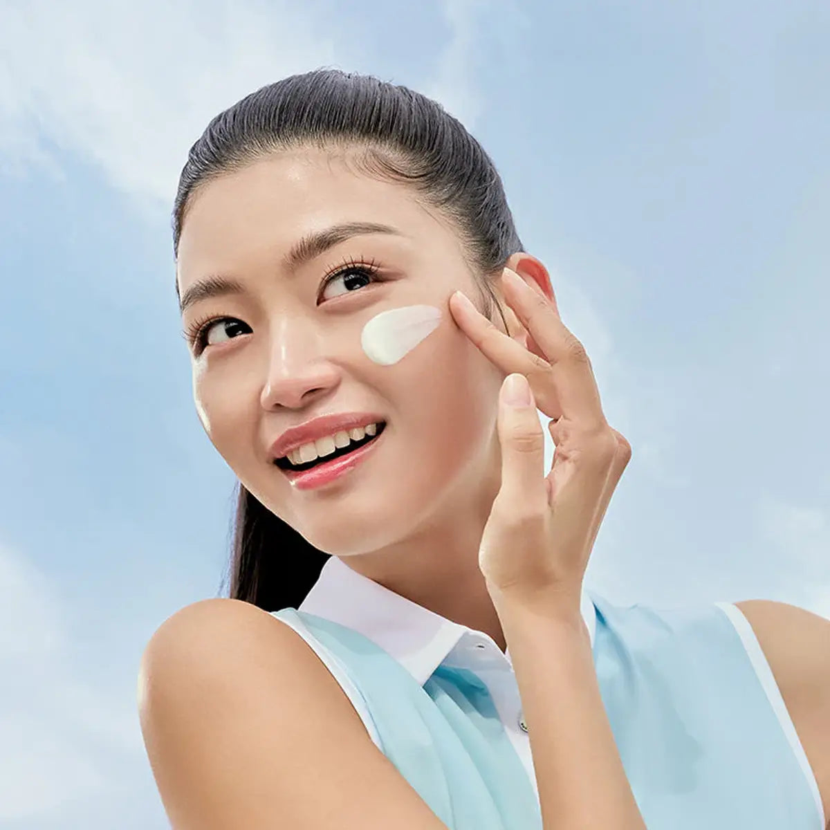Woman applying sunscreen to her face with a light blue background