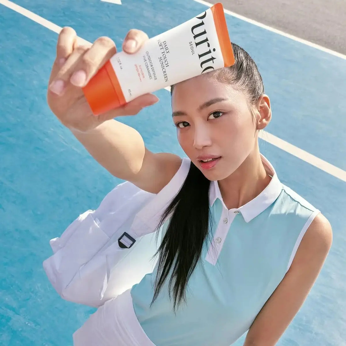 Woman holding a skincare product on a tennis court