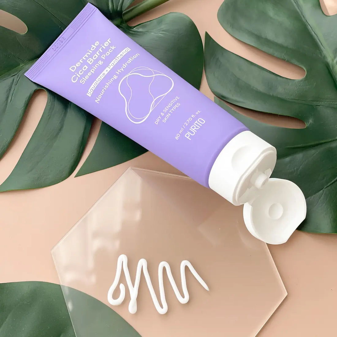 Purple tube of skincare product with white cream on a beige surface with green leaves in the background