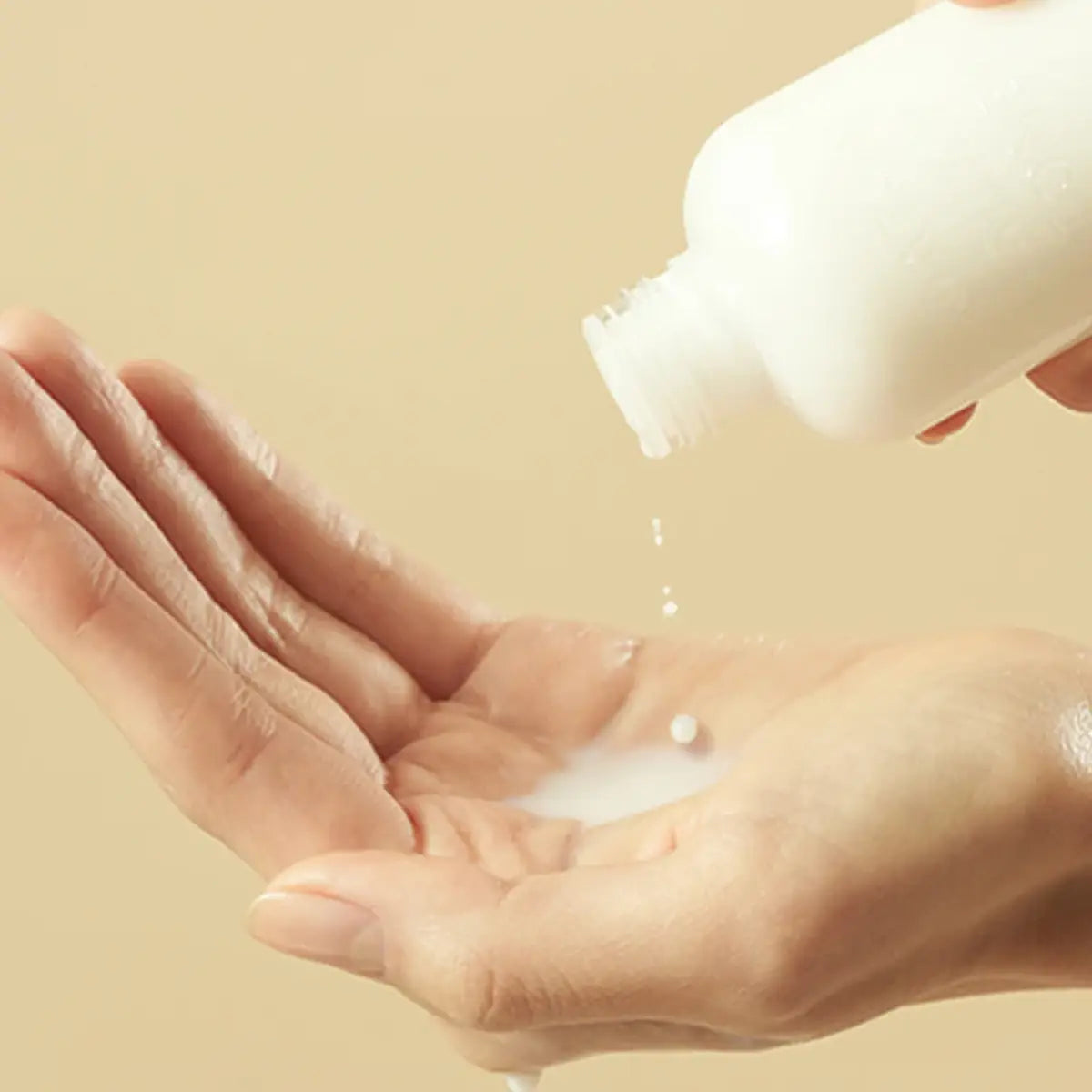 Hand holding a bottle of Purito Oat-in Silky Toner with a beige background