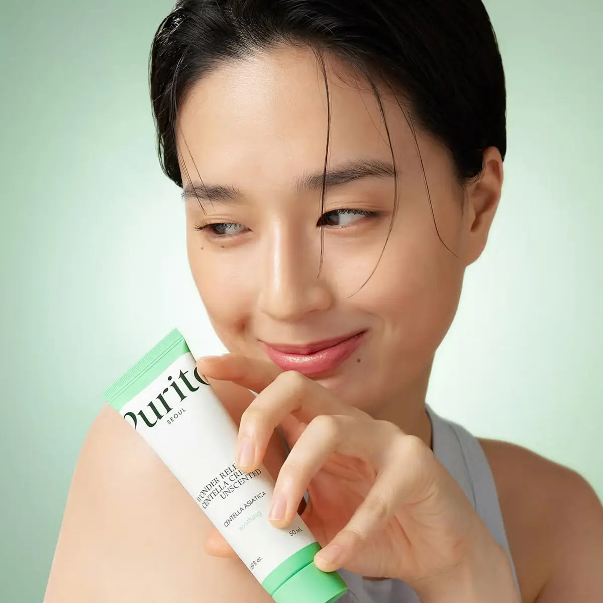Woman holding a skincare product with a green background