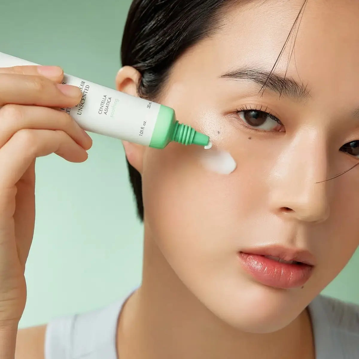 Person applying a skincare product to their face with a green background
