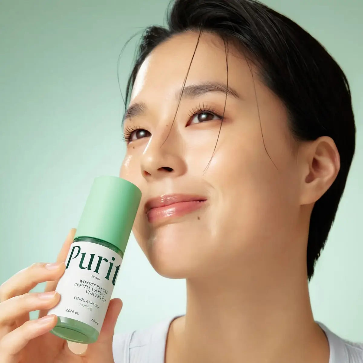Woman holding a green skincare bottle labeled 'Purit' against a light green background