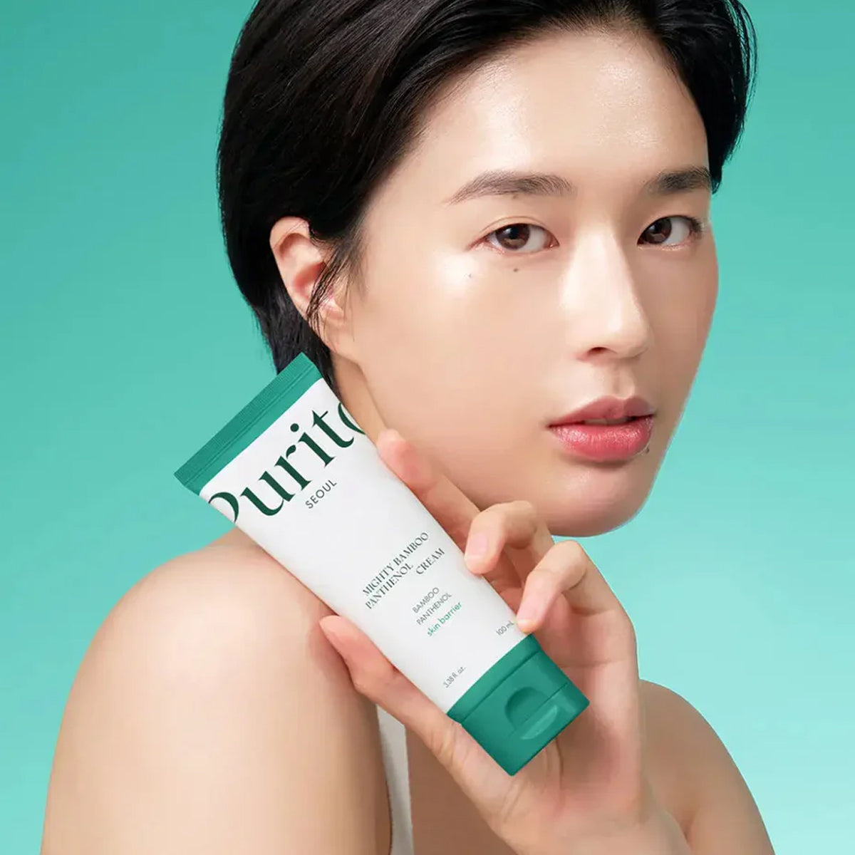Woman holding a tube of Purito skincare product against a teal background