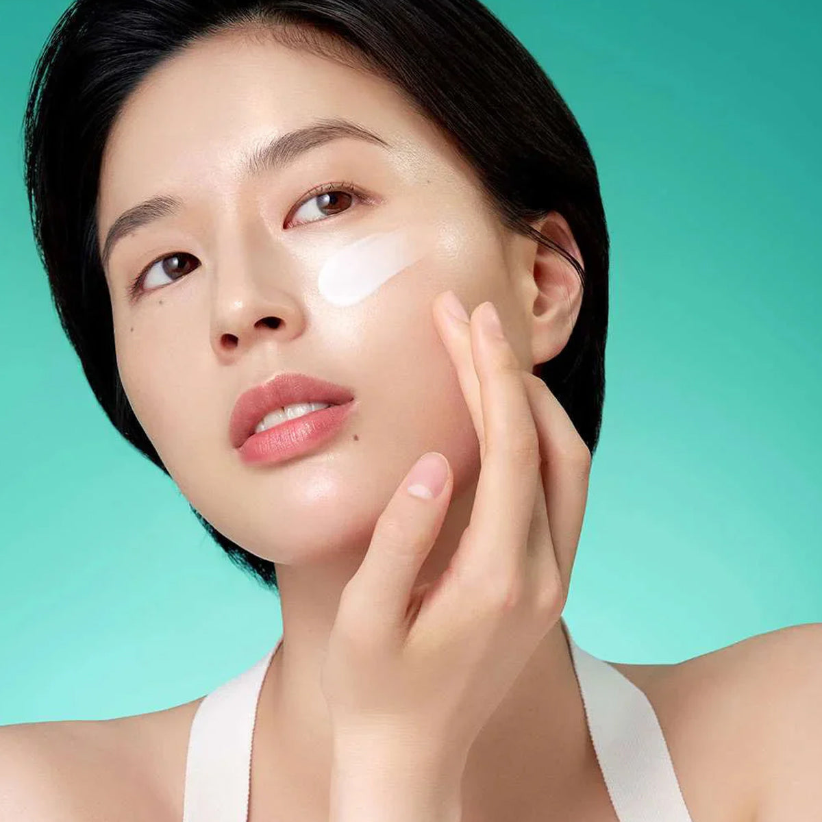Woman applying cream to her face against a teal background