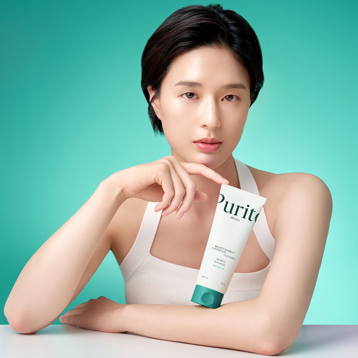 Woman holding a Puriti skincare product against a teal background