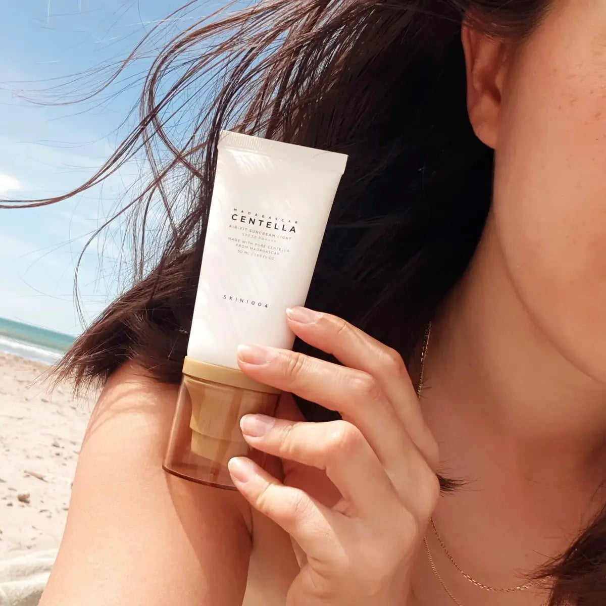 Woman holding SKIN1004 Madagascar Centella Air-Fit Suncream Light tube
