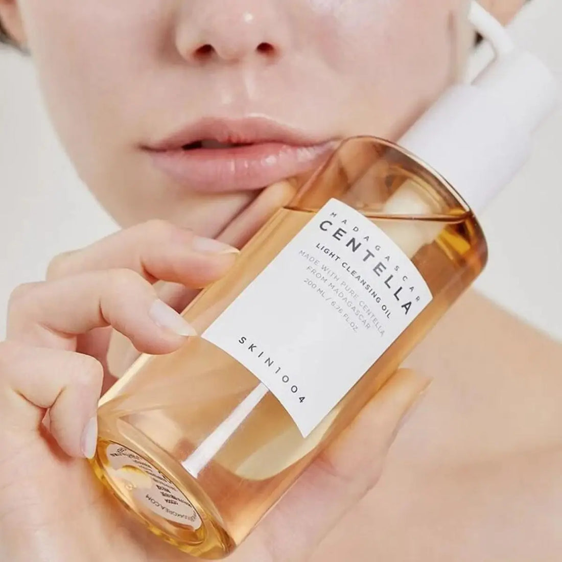 Person holding a bottle of Skinfood Centella Light Cleansing Oil with a close-up of the product.