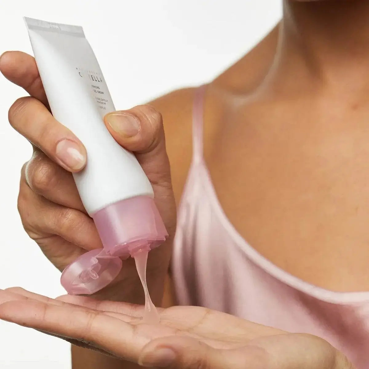 Person holding a skincare product with pink pump and white tube, applying it to their hand.